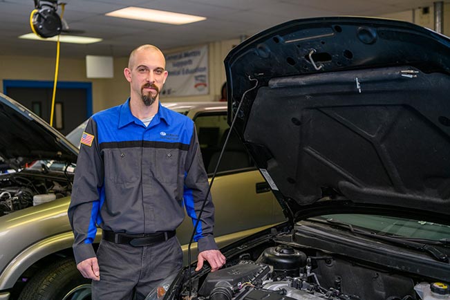 Seth DeGraff standing with hood of car open in automotive lab