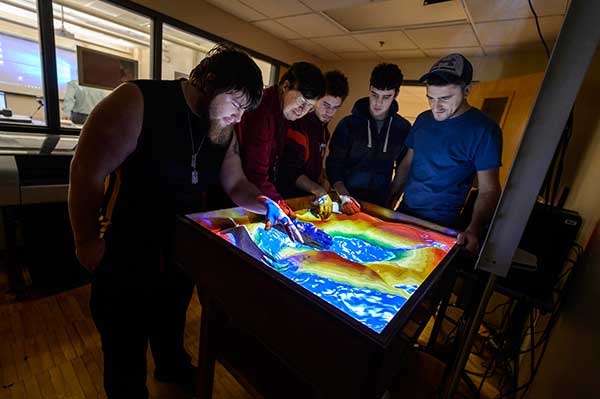 Professor Bill Darling, center, and his students work with the Augmented Reality Sandbox located in Hudson Hall. The sandbox is a new teaching tool that was built by staff and faculty this past summer.