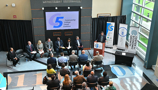 Overhead view of individuals sitting at a press conference with someone speaking at the podium