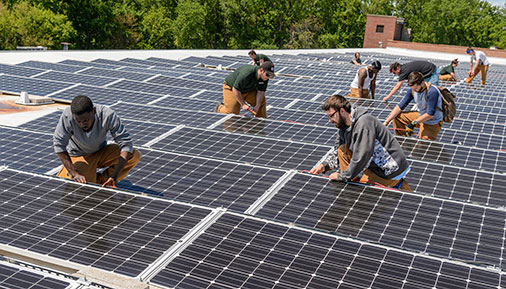 Multiple students working on solar panels on a roof
