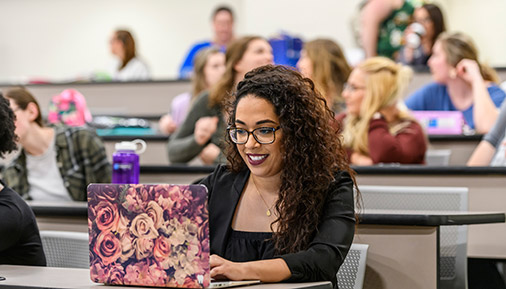 A students works on a laptop in a classroom with other students