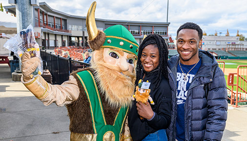 HVCC Viking mascot with two students in the baseball stadium